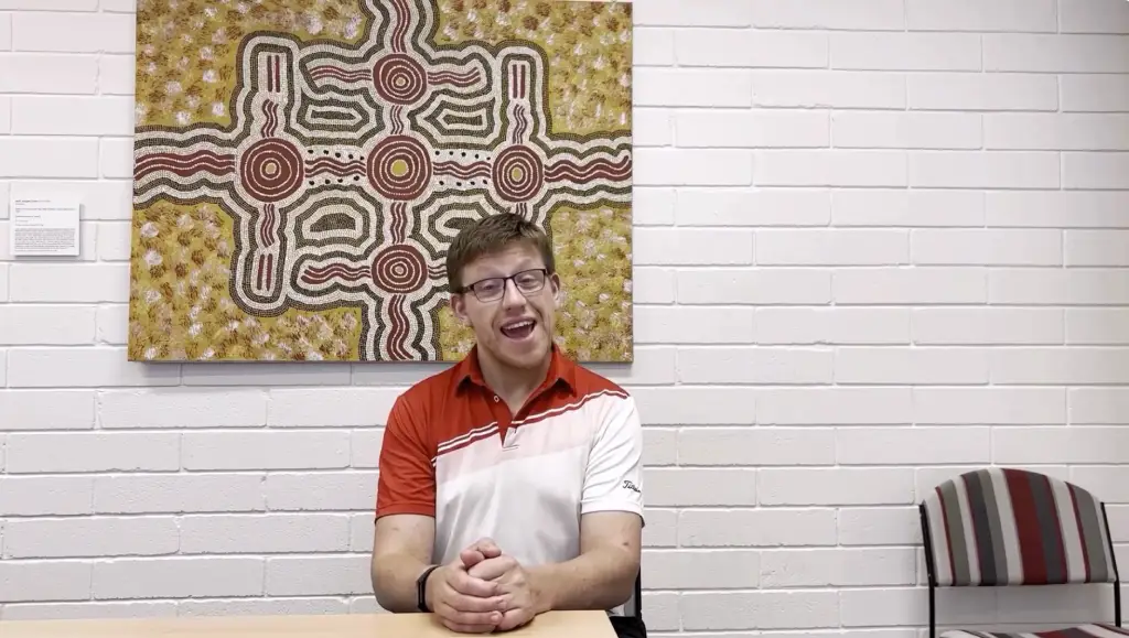 man standing in front of painting talking to camera