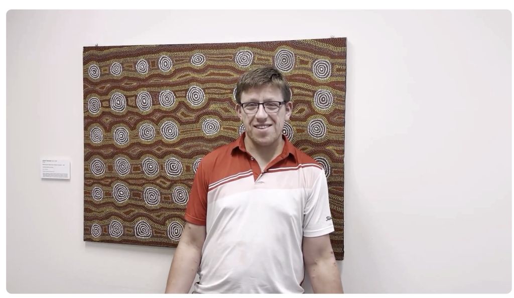 man standing in front of painting talking to camera
